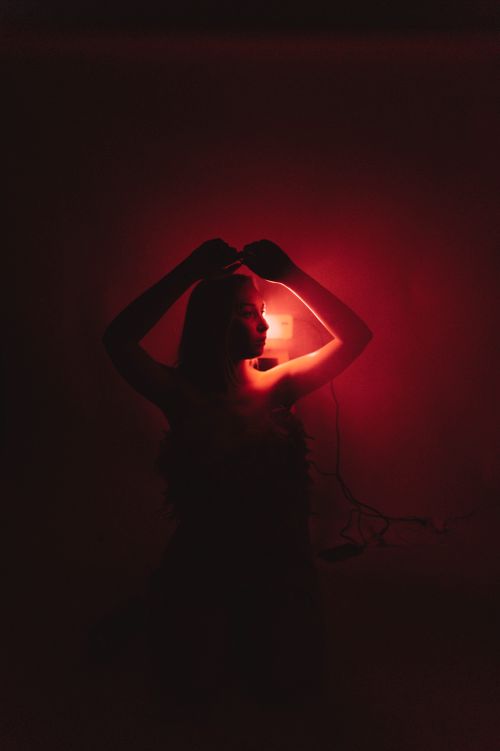 Free Artistic silhouette of a woman with hands raised against a red light backdrop, creating a dramatic and moody atmosphere. Stock Photo