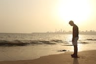 一个年轻人独自站在印度海滩上，身后是日落的天际线