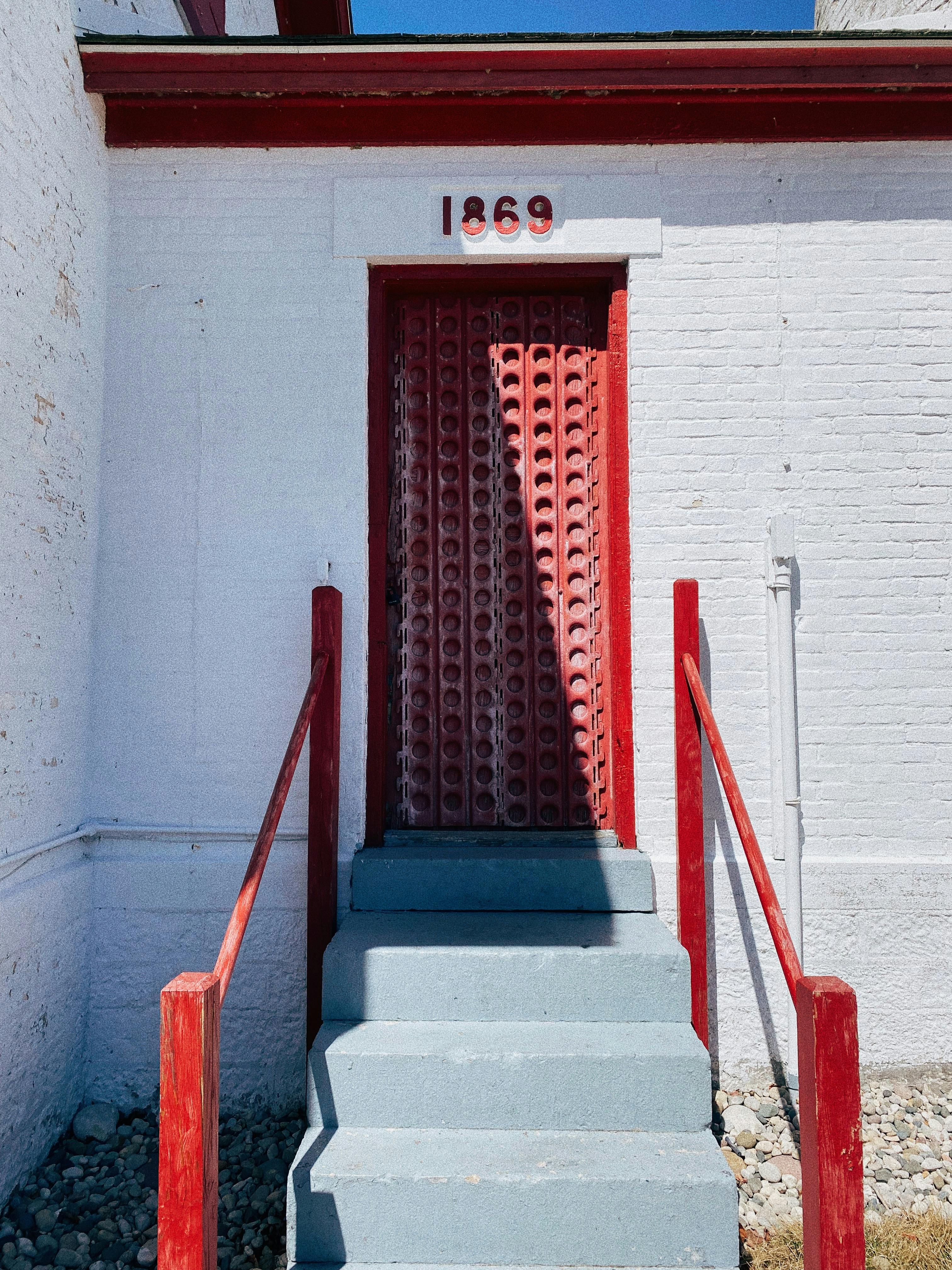 A vintage red door with "1869" above it on a white brick building, showcasing historical architecture.