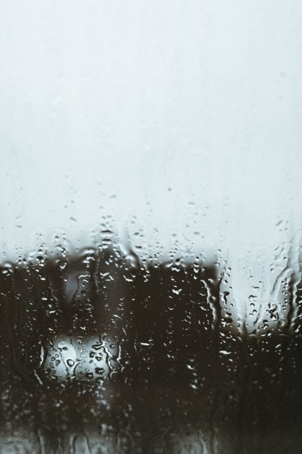 Close-up of raindrops on a window with a blurred outdoor scene, capturing a moody atmosphere.