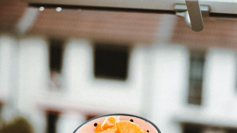 A bowl of fresh orange slices sits on a windowsill during a rainy day, capturing a cozy indoor atmosphere.