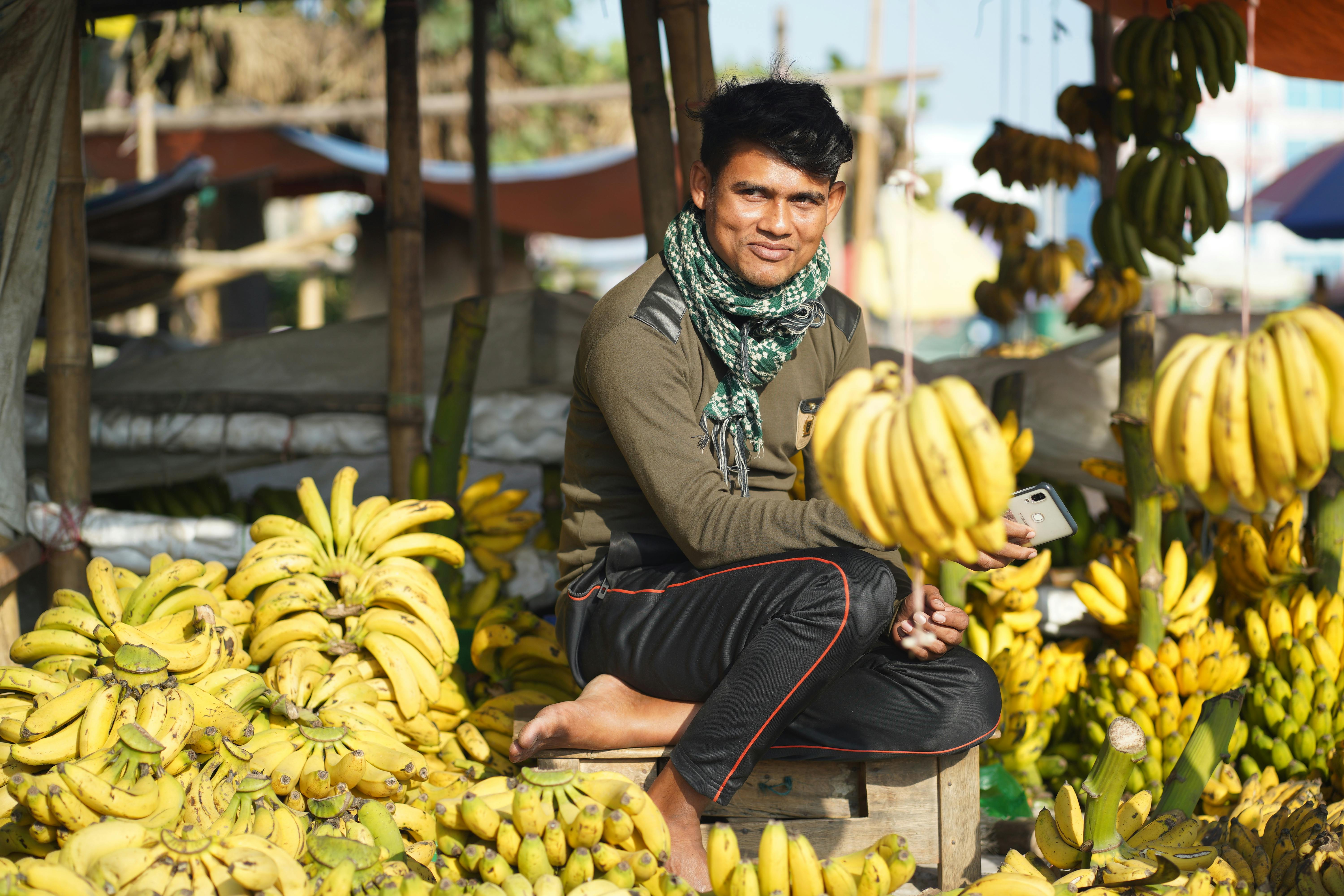 smiling man sitting among bunches of bananas