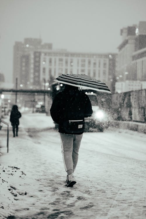 Grayscale Photo of a Person Walking on the Snow Covered Road 