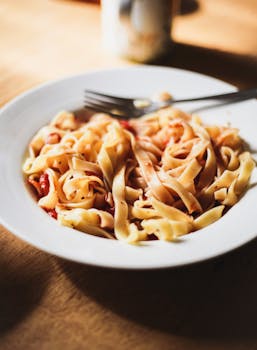 Tasty tagliatelle pasta served in a white bowl with a fork on a wooden table.