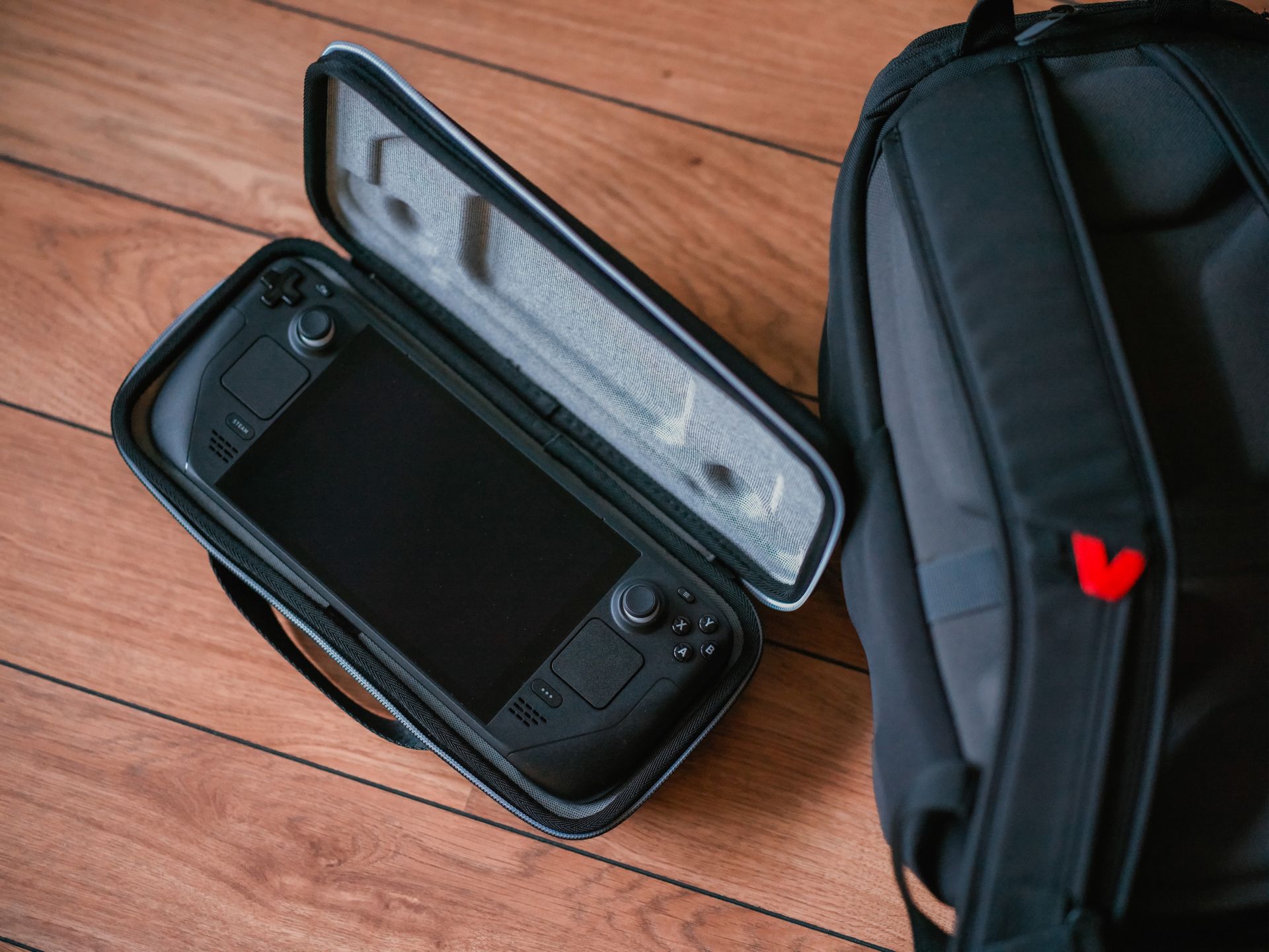A close-up shot of a gaming console in its case next to a backpack on a wooden floor.