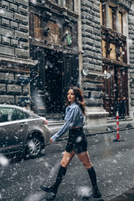 Woman in blue top walking on a snowy street in Turkey, blending fashion with urban winter ambiance.