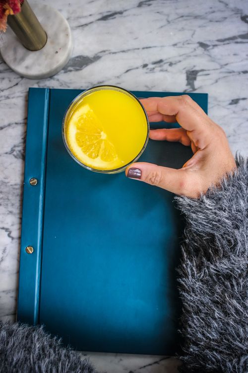 Free A hand holding orange juice over a blue notebook, evoking a cozy and refreshing vibe. Stock Photo