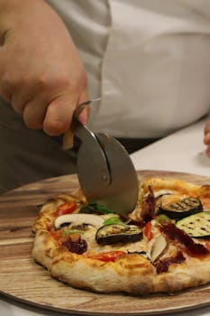 A close-up of a person slicing a homemade vegetable pizza with a cutter.