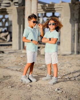 Two boys wearing sunglasses pose confidently under summer sun in Gaza.