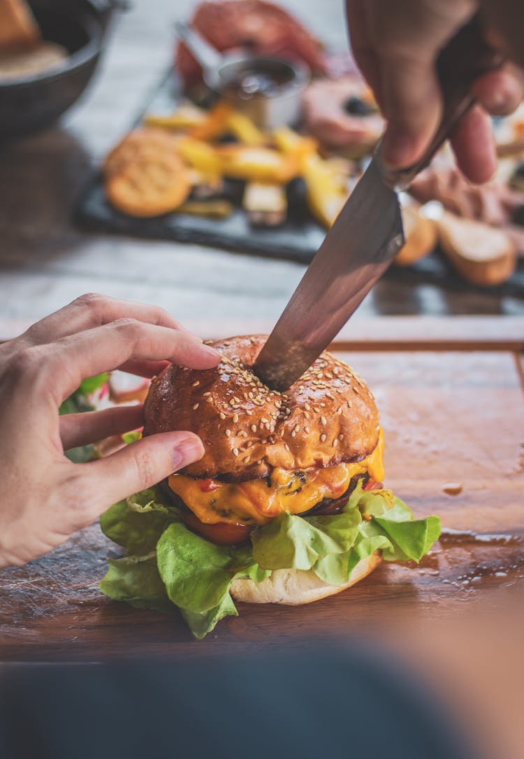 Person Cutting Cheeseburger With A Kitchen Knife