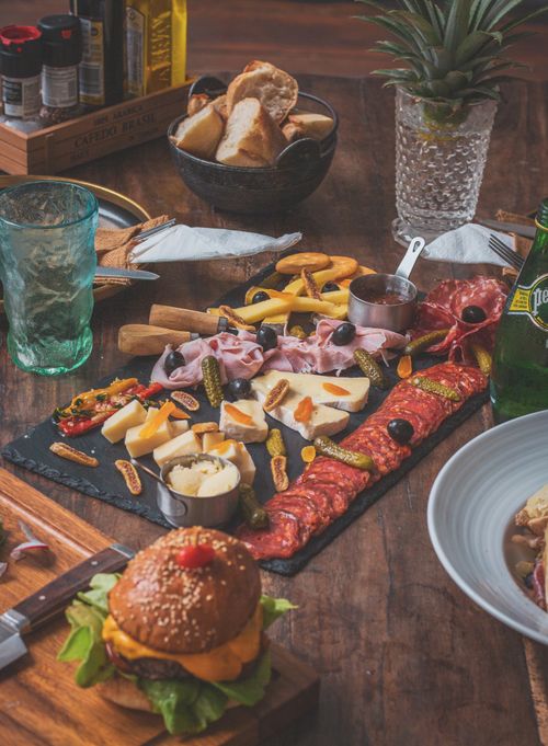 Free Delicious charcuterie board with assorted meats, cheeses, and a gourmet burger on a wooden table. Stock Photo