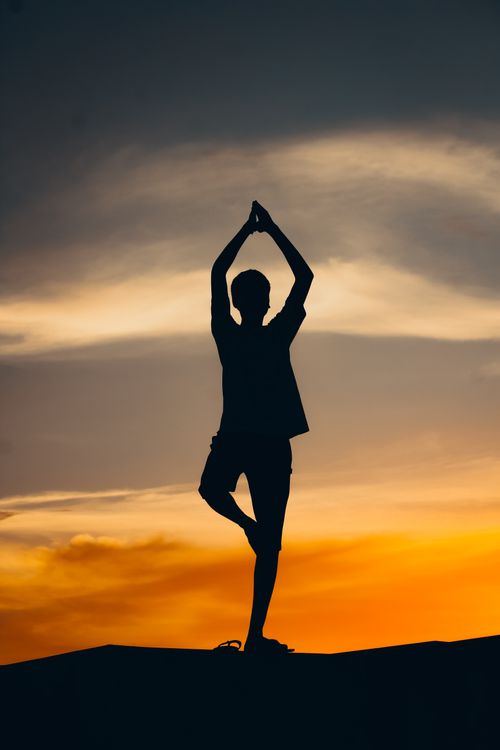 Free A person in yoga pose silhouetted against a vibrant orange sunset in India. Stock Photo