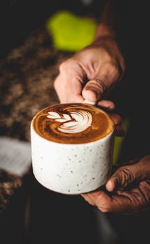 A close-up shot of hands holding a latte with beautiful latte art in a white cup.