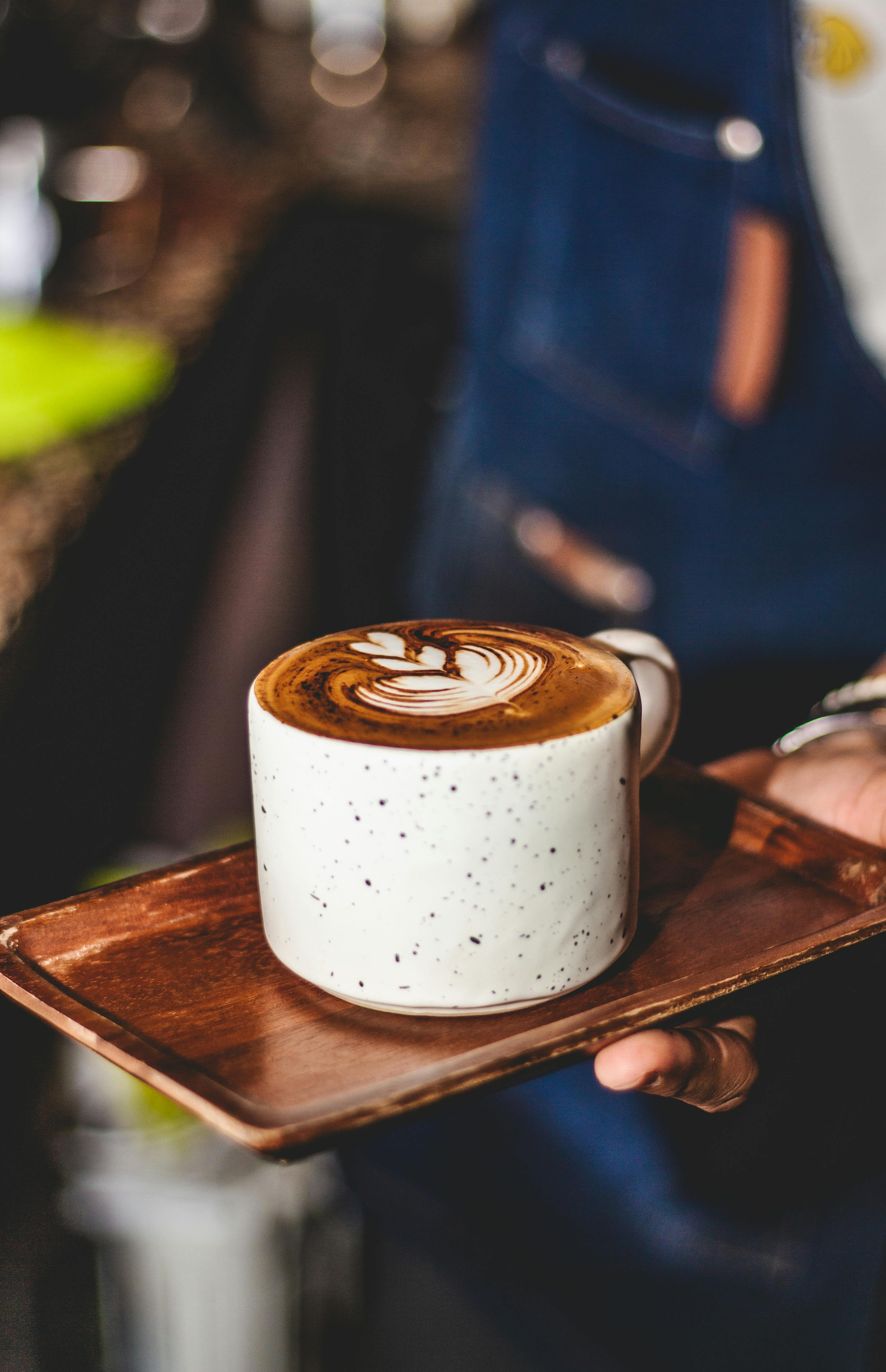 Artistic latte in a speckled mug served by barista, creating a warm café atmosphere.