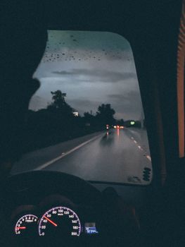 A moody night driving scene, capturing raindrops and highway reflections.