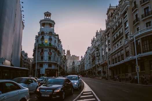 Evening view of traffic on Gran Via in Madrid with historic architecture and city lights.
