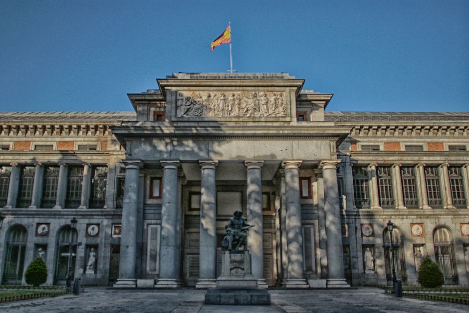 Exterior del Museo del Prado en Madrid con un cielo azul claro y una estatua en frente.
