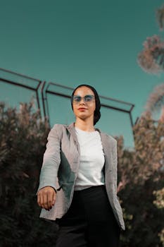 Young woman in fashionable attire standing confidently outdoors under clear sky.