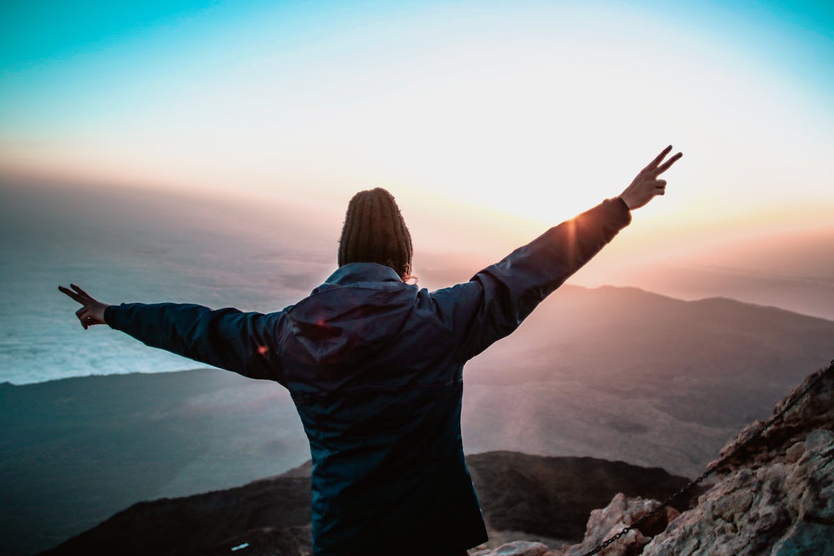Achievement & Motivation – Person Standing on Mountain at Sunset Motivated person standing on a mountain top at sunset, symbolizing success, focus, and achievement