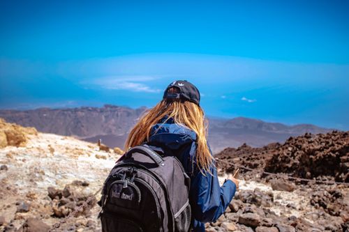 Free Back view of a woman hiking in a rugged volcanic landscape under a clear blue sky. Stock Photo