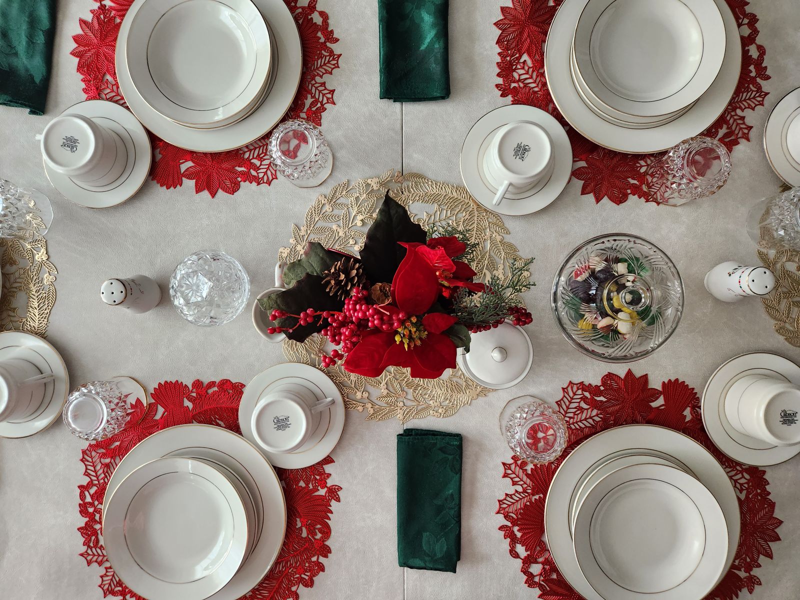 A top view of a Christmas table set with white plates, red placemats, green napkins and a poinsettia centerpiece.
