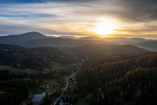Stunning aerial view of forested mountains and a village at sunset, showcasing nature's beauty.