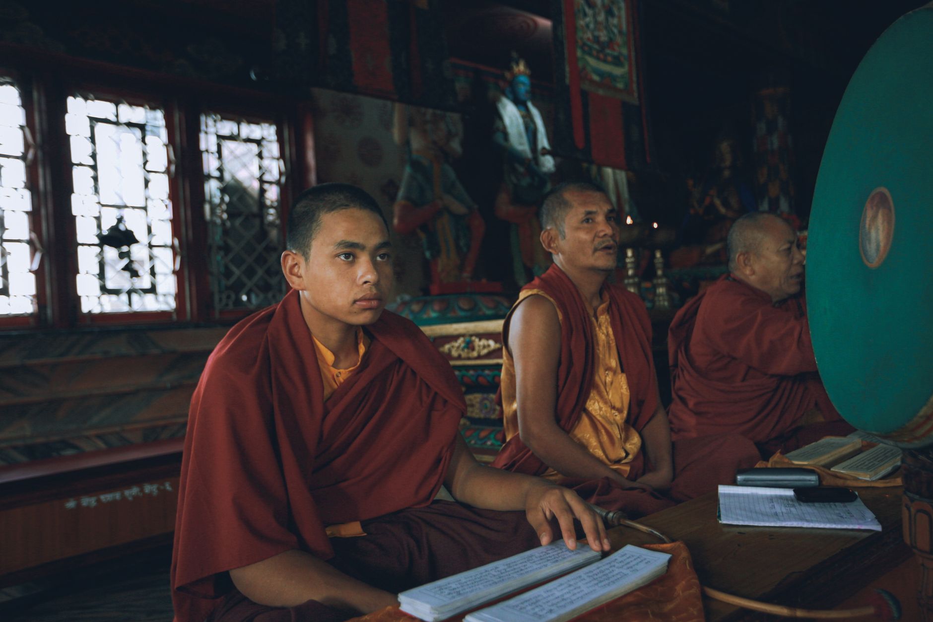 Three monks dressed in orange kasaya robes engaged in spiritual practice inside a buddhist temple.