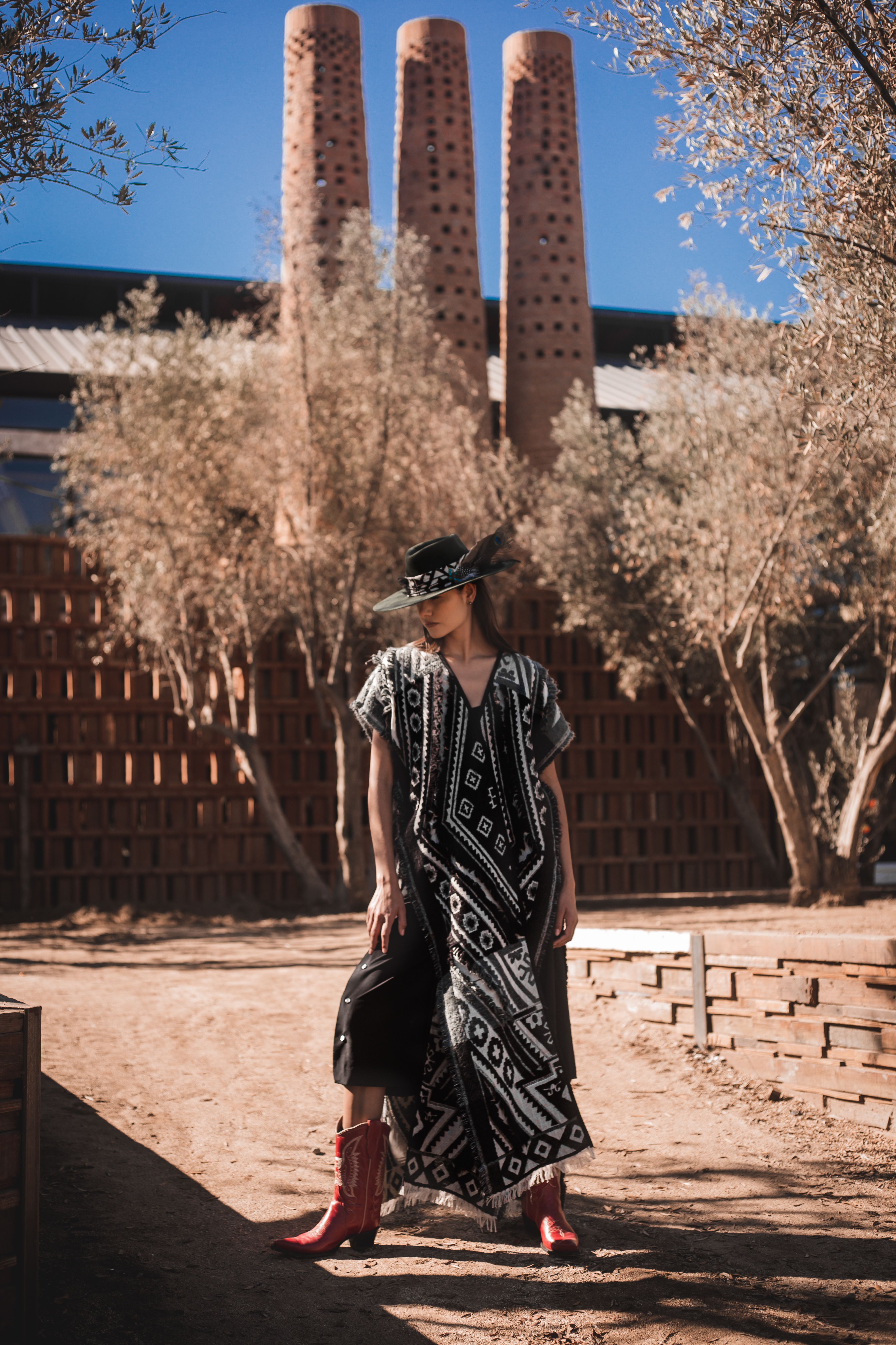 Fashionable woman in a dress and hat posing stylishly outdoors with a unique architectural background.