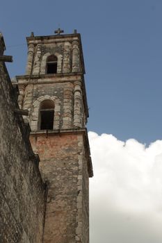 Low-angle view of a historic church bell tower against a blue sky in Valladolid, Mexico.