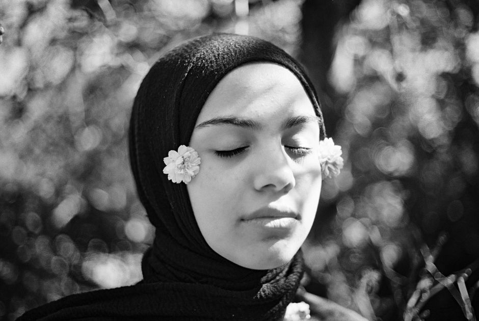 Black and white photo of a woman in a hijab with flowers, eyes closed.