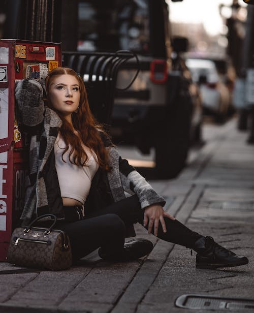 Redhead Woman Sitting on Ground on City Street