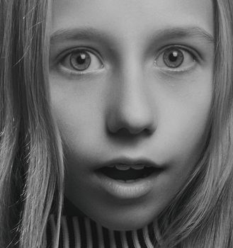 Close-up grayscale portrait of a surprised girl with wide eyes and open mouth.