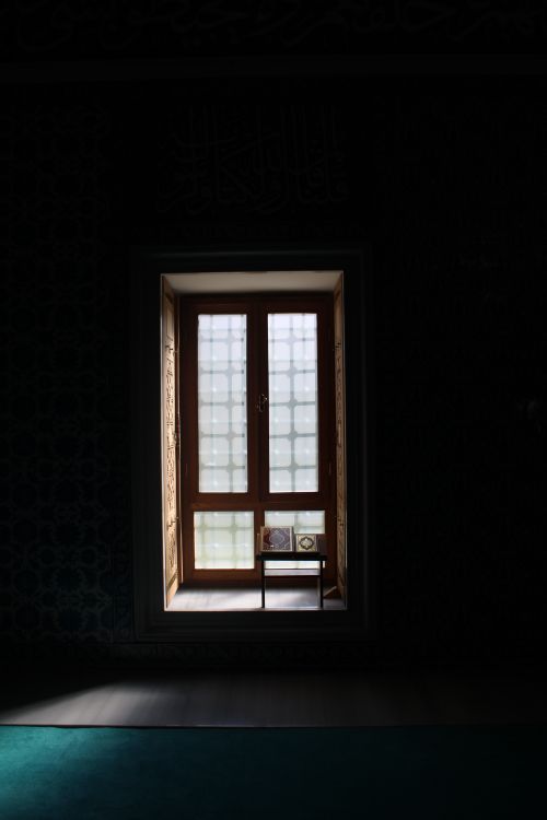 Free A tranquil view of an Islamic window casting soft light into a serene room. Stock Photo