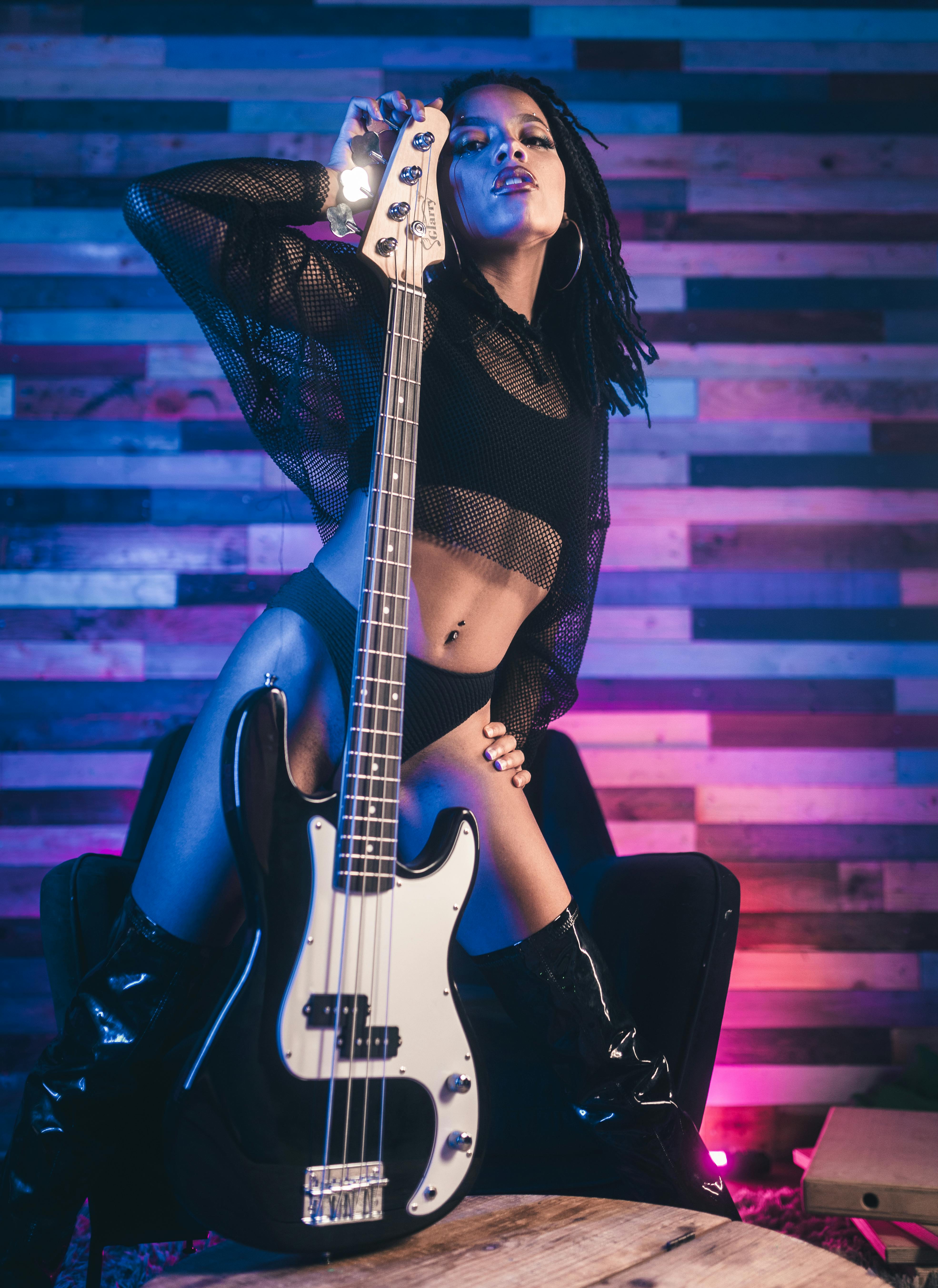 Confident woman in mesh top holding bass guitar in a modern studio setting.