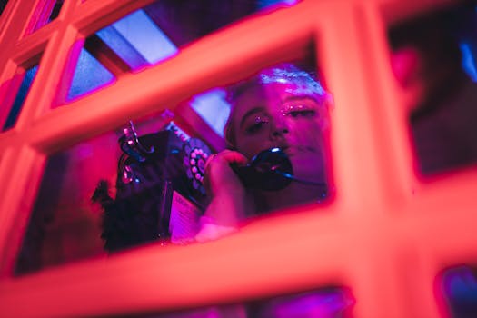 A woman making a call in a neon-lit London phone booth at night, artistic urban vibes.