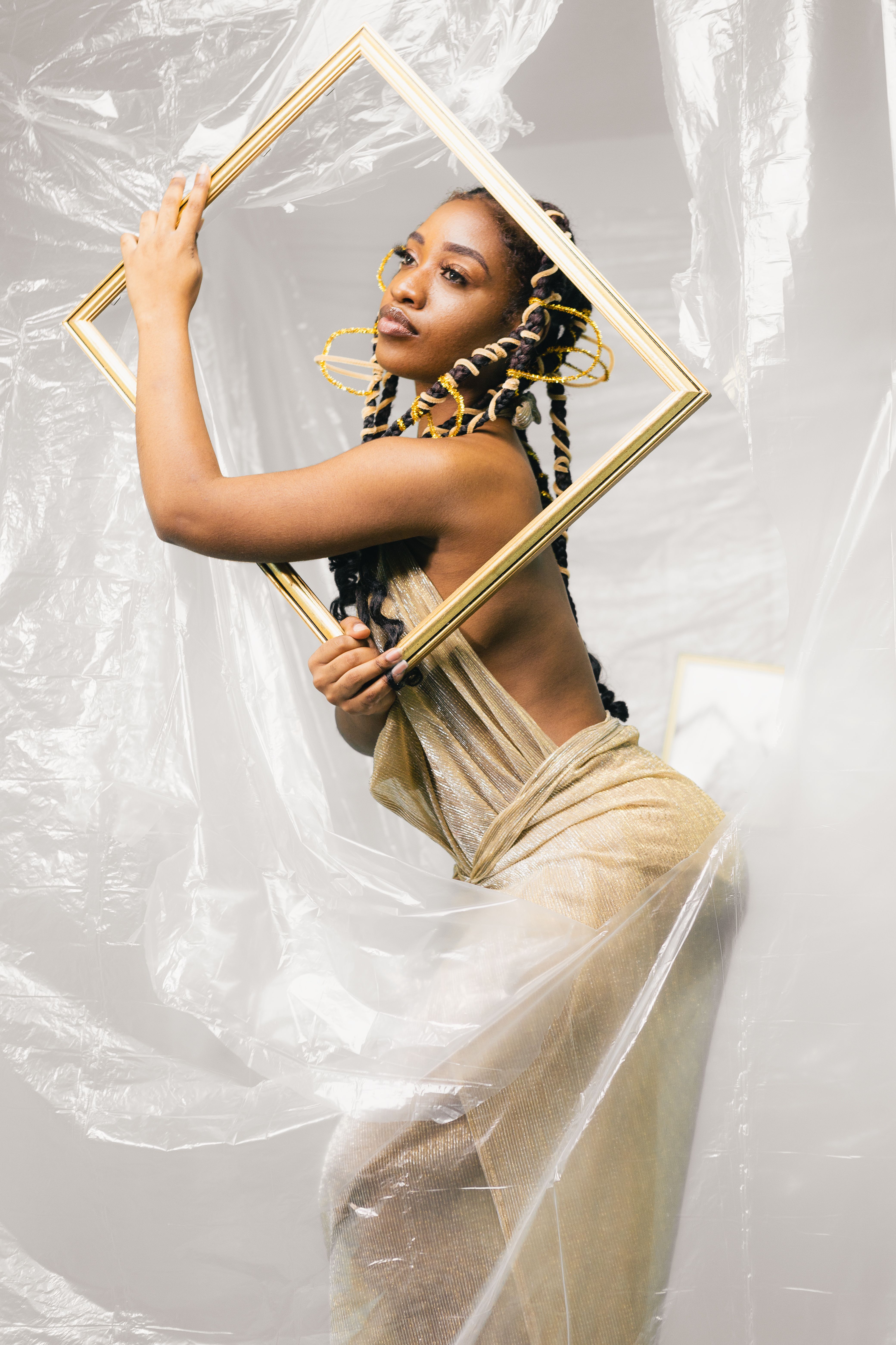 Stylish portrait of a woman posing with a frame, wearing a flowing dress with intricate hairstyles.