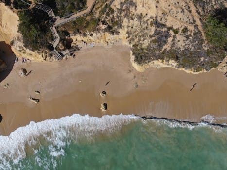 A stunning aerial view of the sandy beach and rocky coastline in Albufeira, Portugal under clear skies.
