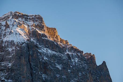 A stunning view of a rugged snow-capped mountain illuminated by sunrise light against a clear blue sky.
