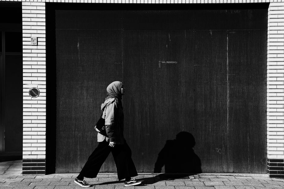Black and white photo of a woman in hijab walking by a wall. Perfect for urban, fashion, or cultural themes.