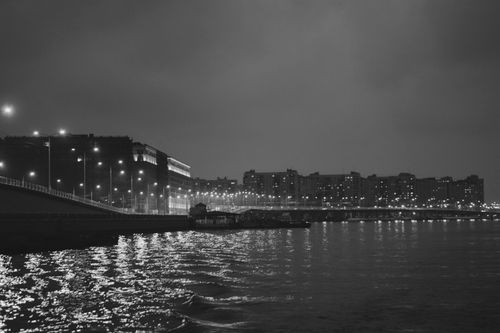 Free Black and white cityscape at night featuring illuminated waterfront and bridge. Stock Photo