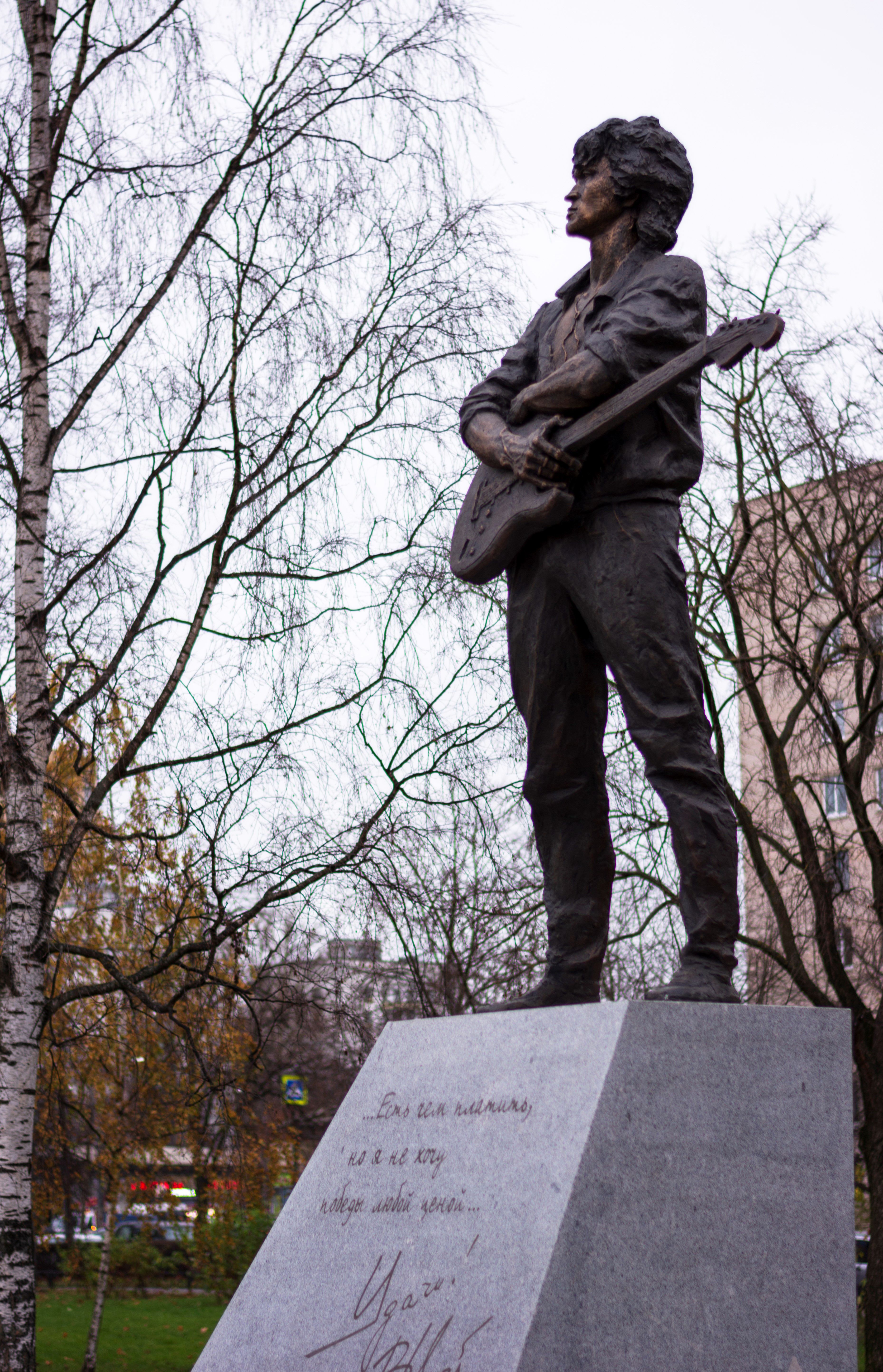 Statue of a musician with a guitar in an urban park setting.