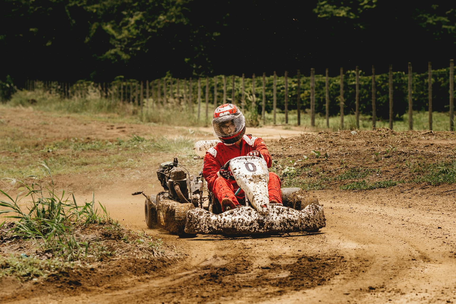 Thrilling off-road kart racing with driver maneuvering through muddy, unpaved track under sunlight.