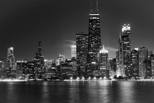 Dramatic black and white view of Chicago skyline illuminated at nighttime reflecting over the water.