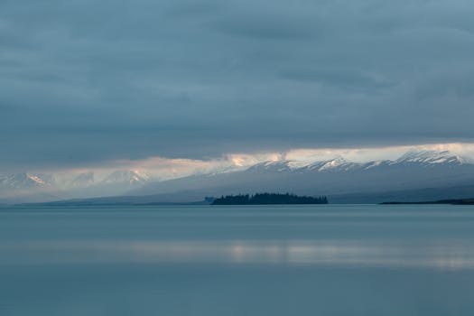 Peaceful lake with snow-covered mountains and cloudy sky.