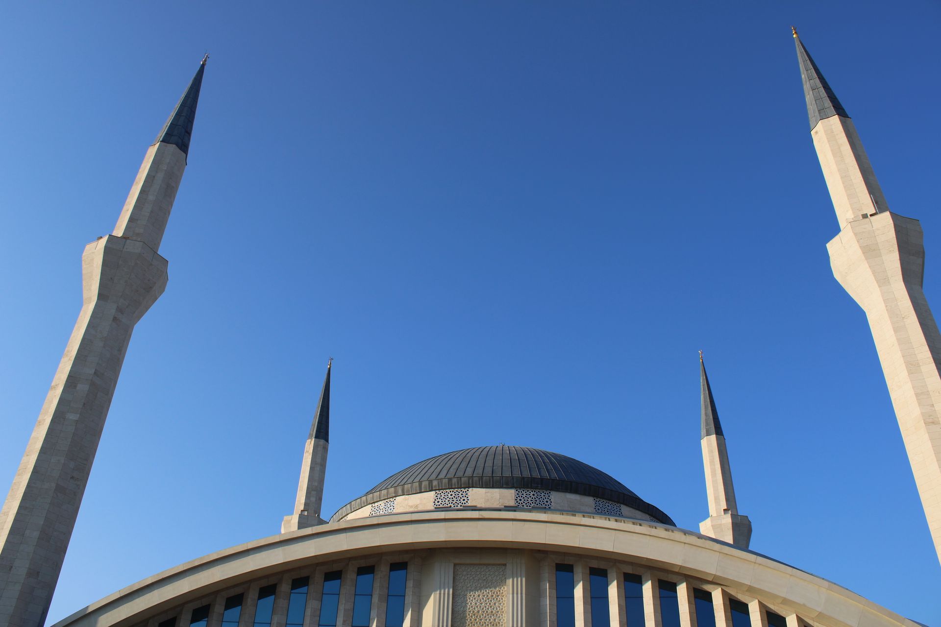 A modern mosque with minarets against a clear blue sky, capturing Islamic architecture beauty.