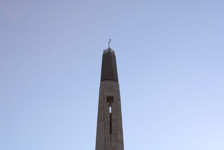 Islamic minaret with crescent symbol set against a clear blue sky, showcasing cultural architecture.