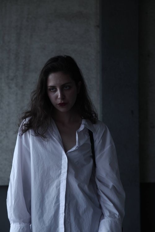 Free A moody portrait of a woman wearing a white shirt in a dark indoor setting. Stock Photo