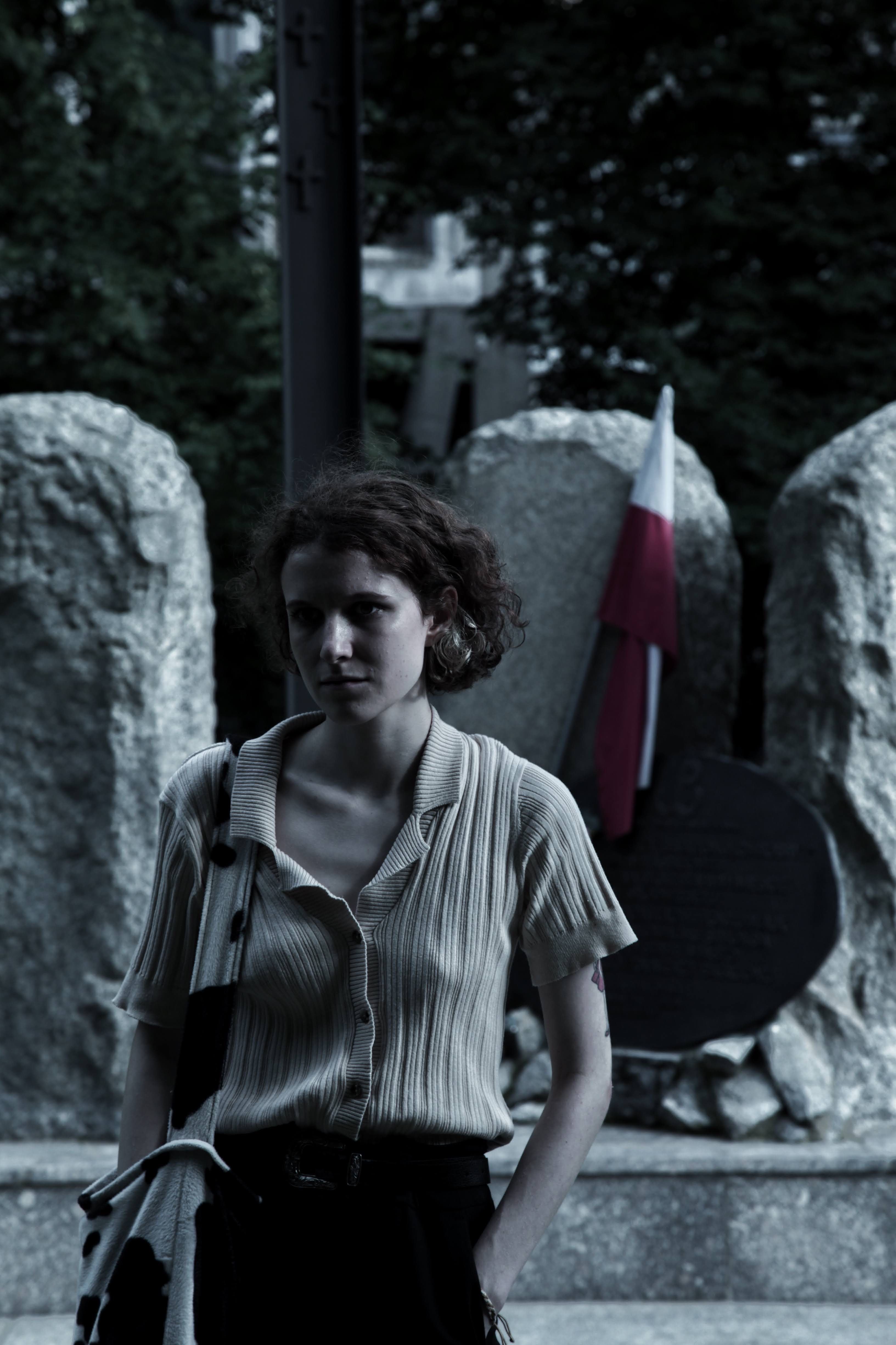A contemplative woman stands near a Polish monument, evoking a sense of reflection.