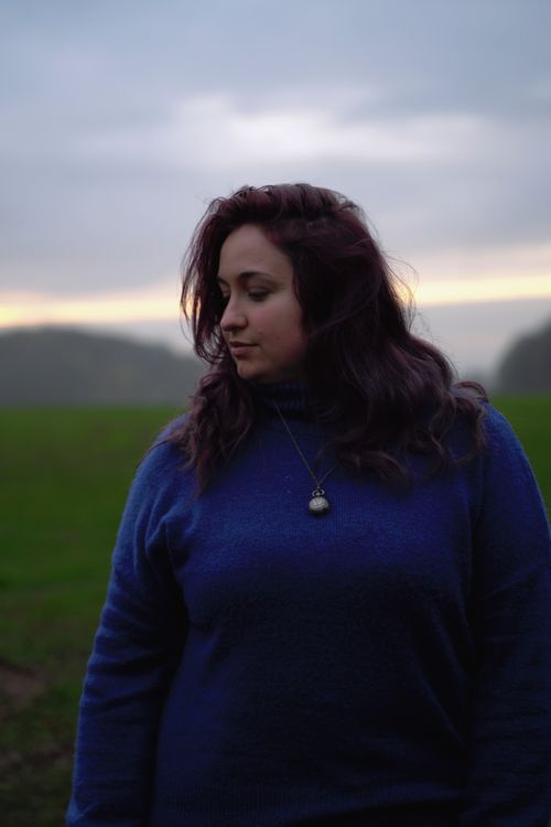 Free A contemplative woman in a blue sweater poses outdoors at twilight. Soft lighting enhances the serene mood. Stock Photo