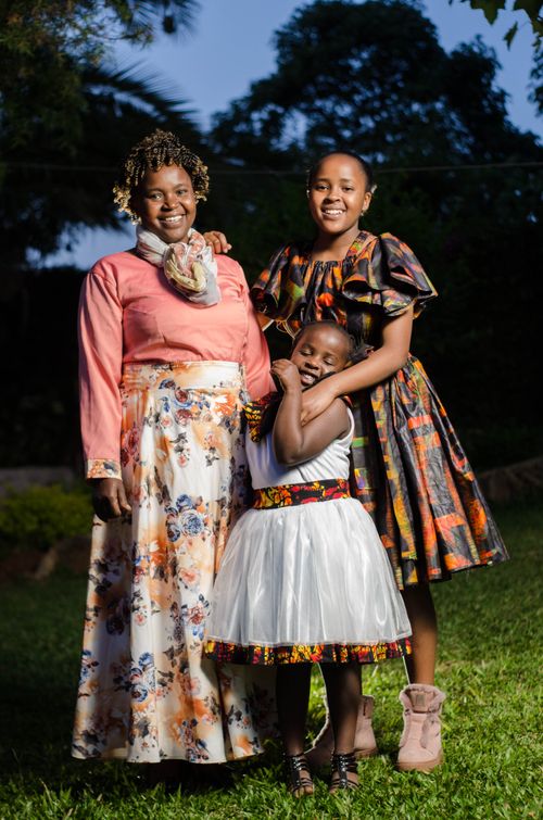 Free A happy family portrait of three smiling women in colorful dresses outdoors, embracing and enjoying the moment. Stock Photo